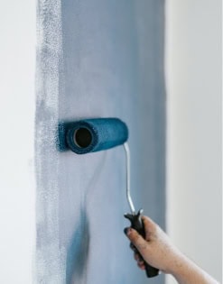 Person using a paint roller on a wall, close-up shot.