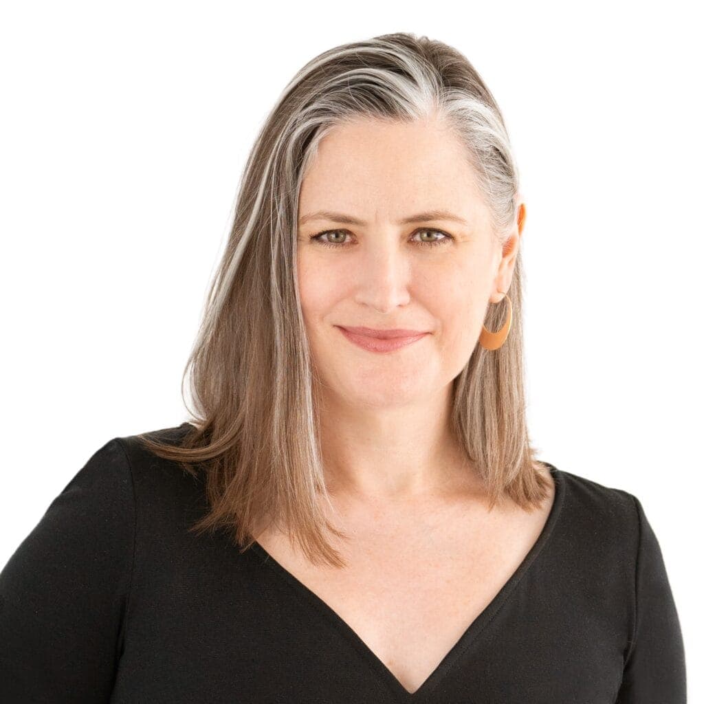 A portrait of Abigail Davis, a professional woman with shoulder-length gray hair, wearing a black top and gold earrings.